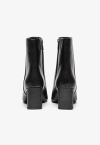 Μαύρες δερμάτινες μπότες μέχρι τον αστράγαλο με ψηλό κομψό τακούνι, με λεία υφή, πλευρικούς φερμουάρ και μινιμαλιστικό σχέδιο στο πίσω μέρος.