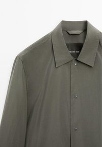 Mørkegrøn skjorte med spids krave, frontlukninger med trykknapper og en glat tekstur. Etiket læser "Massimo Dutti" under kraven.