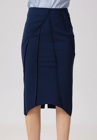 Jupe crayon bleu marine avec une finition texturée, présentant un ourlet asymétrique, des coutures apparentes et une fente incurvée à l'arrière pour faciliter les mouvements.