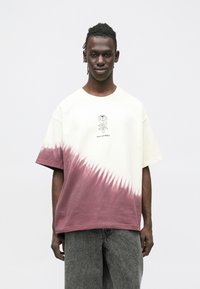 T-shirt z krótkim rękawem w kremowo-bordowy wzór tie-dye z graficznym motywem kwiatu. Luźny krój, miękki bawełniany materiał, minimalistyczny styl.