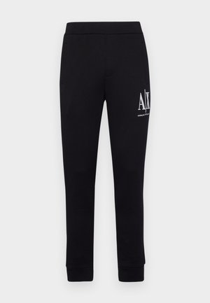 Pantalons de jogging noirs en tissu doux, avec une coupe ajustée, une taille élastique et un texte logo blanc sur la jambe gauche.