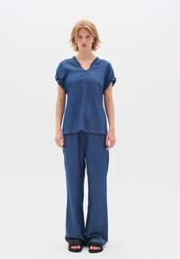 Denimový outfit pozostávajúci z blúzky s krátkym rukávom a V-výstrihom so volánikmi a voľnými nohavicami, obe v stredne modrej farbe.