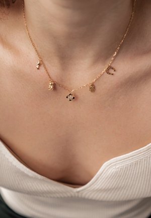 Gold chain necklace featuring multiple charms: a hand, a star, a bear, and a flower with black and white accents. Textured, delicate design.