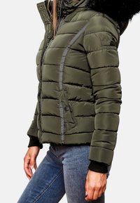 Fyldig, olivengrøn jakke med hætte foret med pels, grå accenter og lynlåslommer. Har ribstrikkede manchetter og quiltet tekstur.