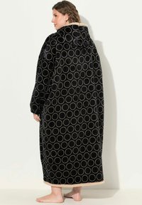 Coperta con cappuccio nera con motivi circolari in crema. Progettata in forma lunga, presenta un tessuto morbido e un colletto foderato in sherpa.