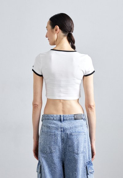 T-shirt branca cropped com bainhas das mangas em preto, combinada com calças cargo texturizadas em azul claro. Costura visível e bolsos traseiros nas calças.