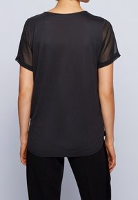 Svart t-shirt med korta, genomskinliga ärmar och rund halsringning. Mjuk tygkvalitet med rak skärning, som sträcker sig något förbi höfterna.