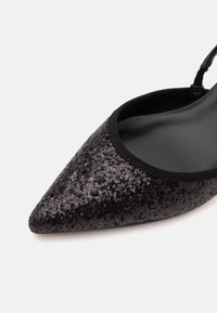 Chaussure plate noire à bout pointu recouverte de petits sequins brillants avec une bride slingback et une doublure intérieure lisse.