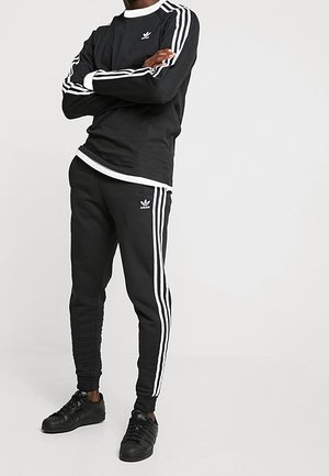 Camiseta deportiva negra de manga larga con detalles y rayas blancas, combinada con pantalones negros ajustados a juego y zapatillas negras con diseño texturizado.