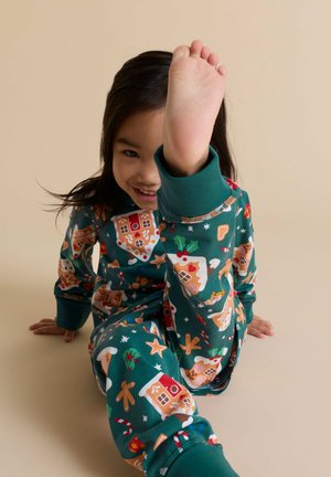 Groene katoenen pyjama's met peperkoekhuisjes en feestelijke patronen, in een ontspannen pasvorm, met omgeslagen mouwen en een speelse pose.