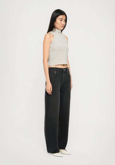 Haut rayé sans manches et court en gris clair et gris foncé ; jean noir taille haute à jambes larges ; chaussures blanches pointues ; fond neutre.