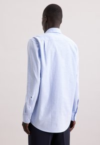 Camicia a quadri blu e bianca, con maniche lunghe, colletto e polsini con bottoni. Tessuto leggero con una consistenza liscia e orlo arrotondato.