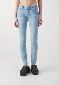 Světle modré skinny džíny s pěti kapsami a zapínáním na knoflík, spárované s černými dřeváky s ventilačními otvory a silným podpatkem.