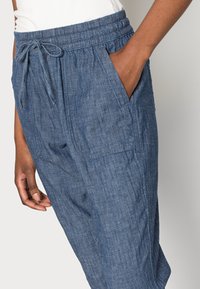 Pantalons en chambray bleu avec une taille élastique et un cordon de serrage. Comprend des poches latérales et un tissu léger et texturé.