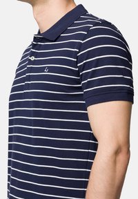 Niebiesko-biały polo w paski z kołnierzykiem, krótkimi rękawami i małym logotypem na piersi. Wykonane z teksturowanej bawełny.