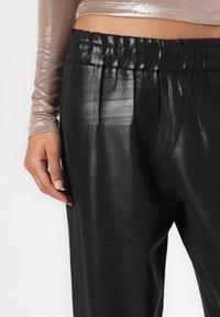 Zwarte, high-waisted broek met een glanzende afwerking, voorzien van een elastische tailleband en plooien, gecombineerd met een metallic lange mouw top.