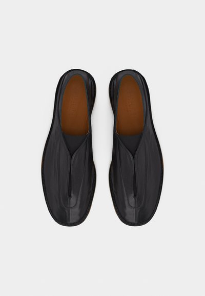 Paire de chaussures noires en cuir à enfiler, avec un bout carré arrondi et une doublure intérieure marron, présentées côte à côte sur fond blanc.