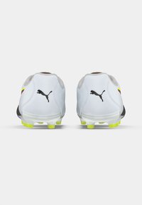 White football boots with black Puma logo, yellow accents, and cleats. Smooth material with a rounded toe and cushioned heel.