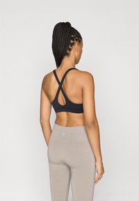 Μαύρο αθλητικό σουτιέν με σχέδιο διασταυρούμενης πλάτης και κομμάτι κοπής, συνδυασμένο με μπεζ κολάν που διαθέτουν subtil λογότυπο στη ζώνη.