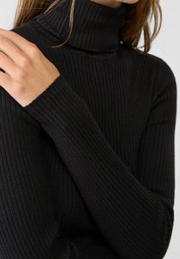 Pull en maille côtelée noir avec col roulé, fabriqué dans un matériau doux et texturé. Il est doté de longues manches et d'une silhouette ajustée.