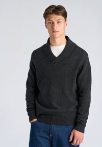 Dunkelgrauer Pullover mit Schalkragen, gerippten Bündchen und Saum sowie lockerer Passform; getragen über einem weißen T-Shirt und kombiniert mit blauen Jeans.