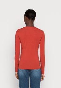 Lange mouwen, roestkleurig shirt met een ronde halslijn en een zachte textuur. Gecombineerd met blauwe jeans, gezien vanaf de achterkant.
