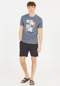 Grå t-shirt med tryckta grafiker som föreställer landskap och texten "Adrenaline Denver Colorado", kombinerad med svarta shorts och bruna sandaler.