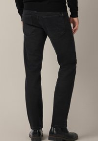 Czarne dżinsy slim fit z denimu, z dwoma tylkimi kieszeniami o subtelnym wzorze szycia. Noszone z czarnymi chelsea.