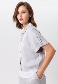 Hellgrau button-up Bluse mit kurzen Ärmeln, ausgestattet mit einem Kragen, seitlichen Taschen und einem gerafften Saum für eine taillierte Passform. Glatte Textur.