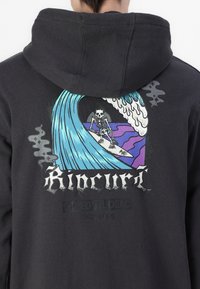Schwarzer Hoodie mit einem Grafikdesign eines Skeletts, das auf einer Welle surft. Verfügt über lebendige Blau- und Lila-Töne und den Text "Rip Curl."