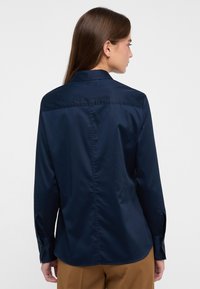 Granatowa koszula z długim rękawem, klasycznym kołnierzykiem, gładką teksturą i mankietami zapinanymi na guziki. Tył koszuli ozdobiony jest centralnym szwem dla dodatkowego akcentu.