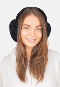 Cache-oreilles en polaire noire avec un design rond, une texture douce et un rembourrage épais. Portés par-dessus une veste en fausse fourrure blanche sur un fond uni.