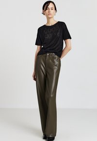 Maglione a maglia con motivo nero e pantaloni a gamba larga in ecopelle verde oliva. L'outfit presenta texture sottili e una silhouette pulita e moderna.