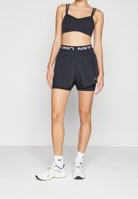 Musta urheiluliivit, joissa on ohut olkain, yhdistettyinä mustiin urheilushortseihin, joissa on joustava vyötärö ja valkoinen Nike-logo. Valkoiset lenkkarit viimeistelevät asun.