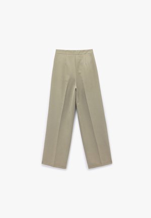 Beżowe spodnie o szerokich nogawkach z gładką teksturą, z wysokim stanem, fałdami z przodu i bez widocznych kieszeni. Ustrukturyzowany fason z wyraźnymi liniami.