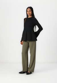 Top peplum nero con maniche lunghe, abbinato a pantaloni a gamba larga verde oliva e scarpe nere con elementi decorativi.
