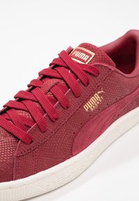 Baskets Puma Basket rouges avec empeigne texturée, lacets assortis, logo doré sur le côté et la languette, et semelle en caoutchouc blanche.