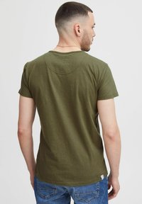 Olivegrünes T-Shirt mit kurzen Ärmeln aus weichem Stoff, mit einem Rundhalsausschnitt und einer dezenten gebogenen Naht auf der Rückseite. Getragen mit blauen Jeans.