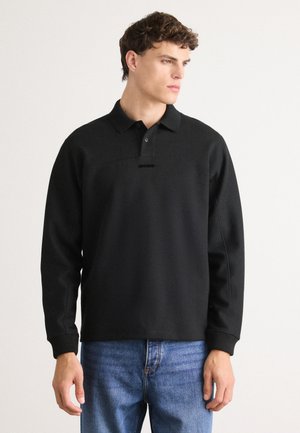 Sweatshirt noir de style polo en tissu doux, avec un col, une patte de boutonnage à trois boutons et un détail de logo discret sur la poitrine.