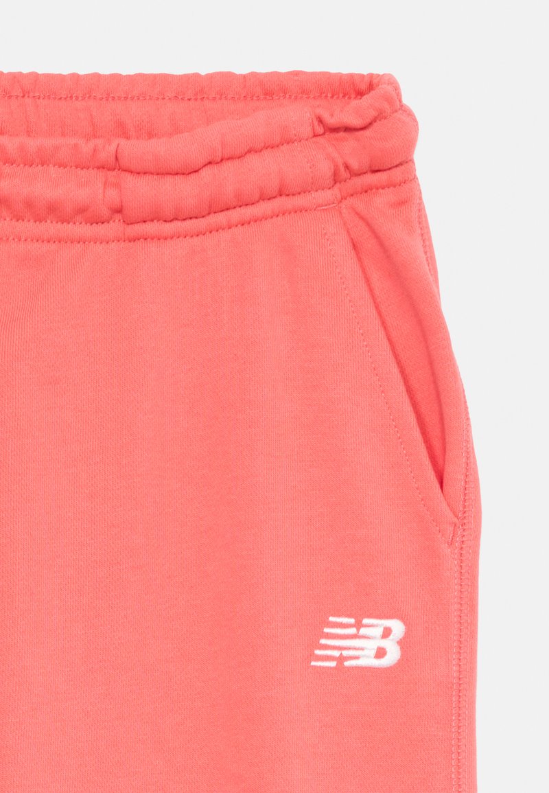 Jogging en corail avec une taille élastique et des poches latérales. Présente un logo New Balance blanc brodé sur la cuisse gauche.