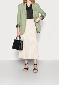 Grön kavaj, svart blus, plisserad krämfärgad kjol, svart handväska. Strappy svarta sandaler med beige sula. Slätt tyg och strukturerad design.