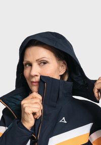 Marineblaue wasserfeste Jacke mit Kapuze, ausgestattet mit orangefarbenen und weißen Streifen, Reißverschluss und strukturiertem Futter. Enthält eine verstellbare Kordel.