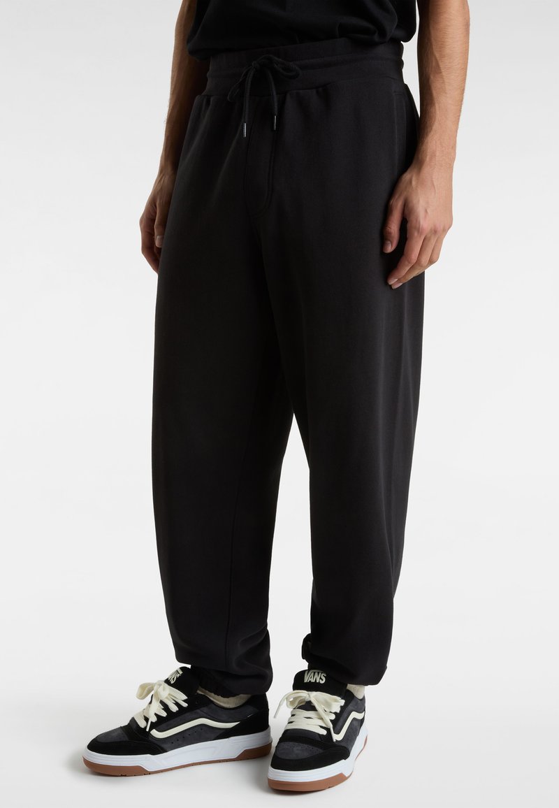 Schwarze Sweatpants mit Kordelzugbund, lockerer Passform und gerippten Knöcheln, kombiniert mit schwarz-weißen Sneakers mit Logo.