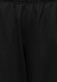Gros plan d'un tissu noir avec une ceinture élastique, montrant des détails de texture froncée et lisse.