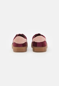 Burgundyröda mockaskor med rosa detaljer och bruna gummisulor. Har förstärkt häl och logodetaljer på baksidan.