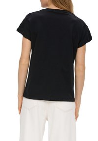 Czarny krótki top z krótkim rękawem z teksturowanymi akcentami z dzianiny na ramionach. Gładki bawełniany materiał, luźny krój i prosty dół. Noszony z jasnymi spodniami.