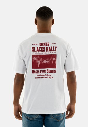 T-shirt bianco in cotone con testo bordeaux sul retro: "DICKIES SLACKS RALLY," dettagli dell'evento e una piccola foto di auto da corsa.