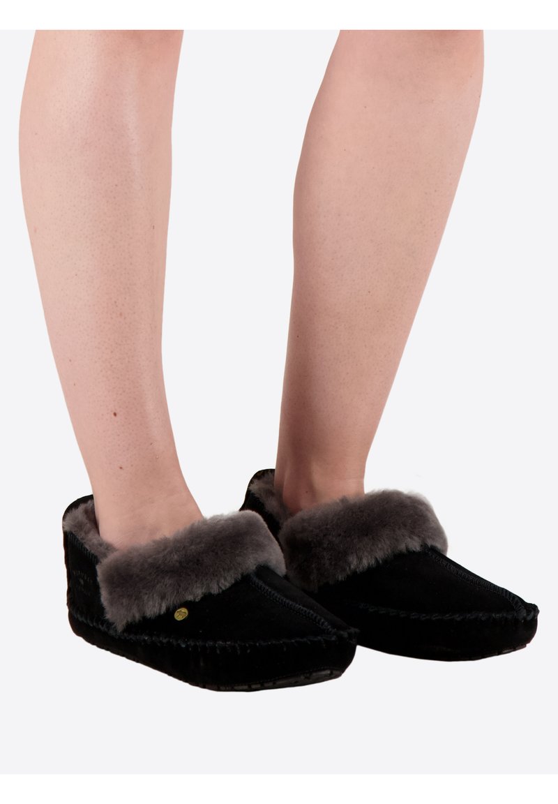 Zwarte pantoffels met een zachte grijze bontvoering, met een puntige neus en decoratieve stiksels langs de rand. De platte zool biedt comfort.