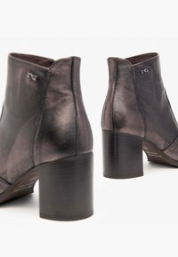 Bottines en cuir de couleur gris métallique foncé, avec un talon carré, une texture lisse, des coutures discrètes et un petit détail de logo.