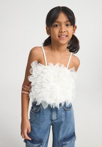 Top senza maniche bianco plissettato in tulle, con spalline sottili, abbinato a pantaloni in denim blu con tasche cargo. Aspetto testurizzato e morbido.